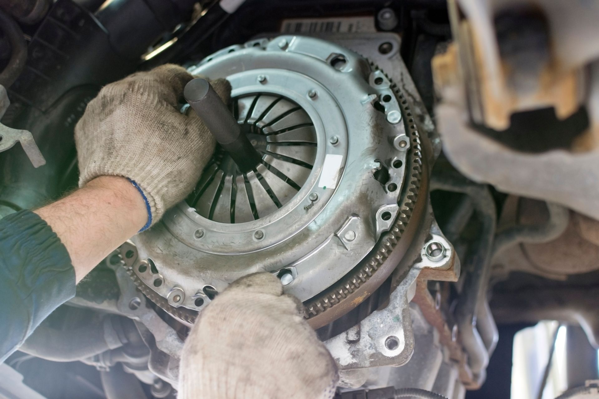 A mechanic wearing work gloves installs a car clutch pressure plate onto an engine flywheel.