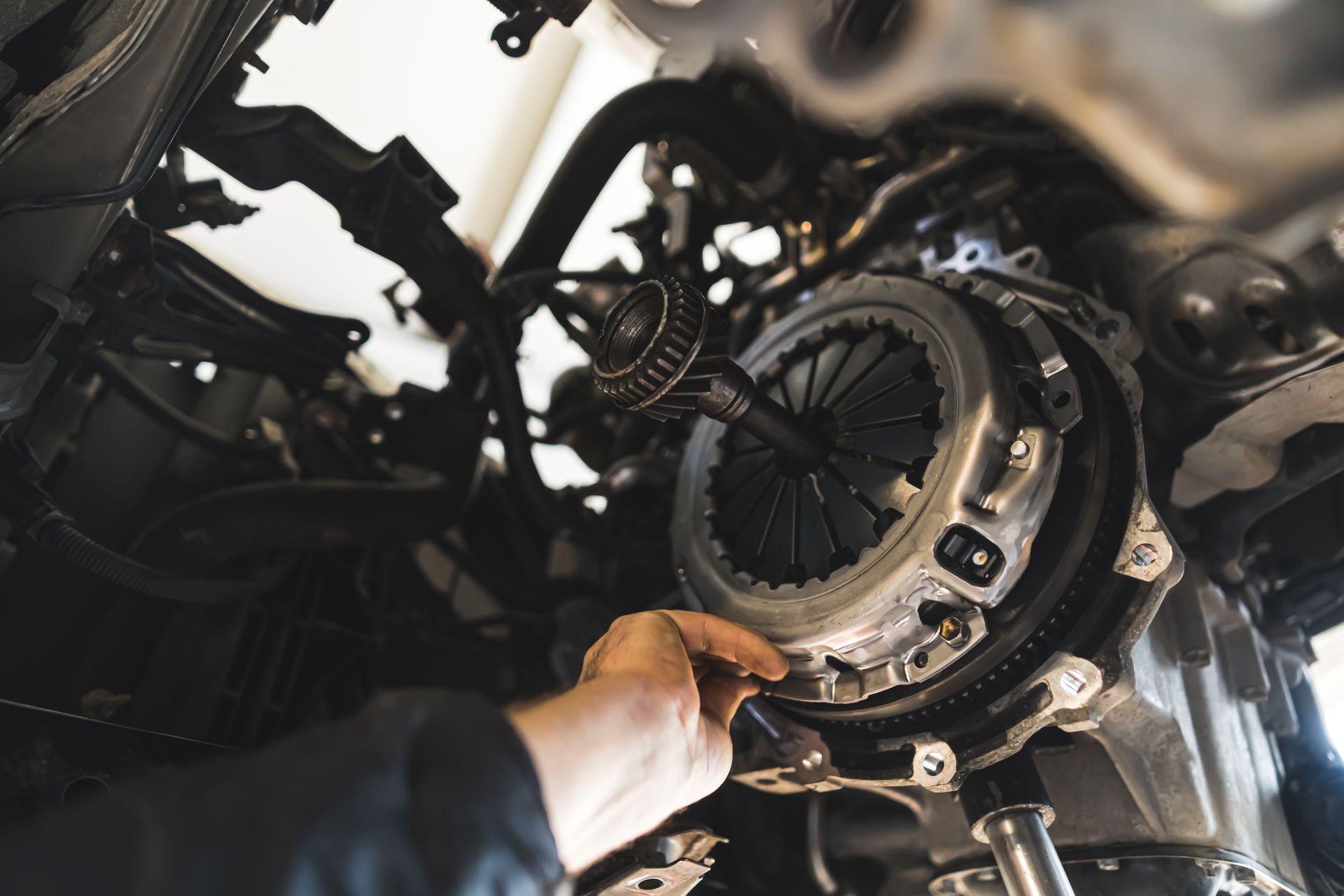 A mechanic's hand works on a clutch assembly attached to a vehicle's engine block.