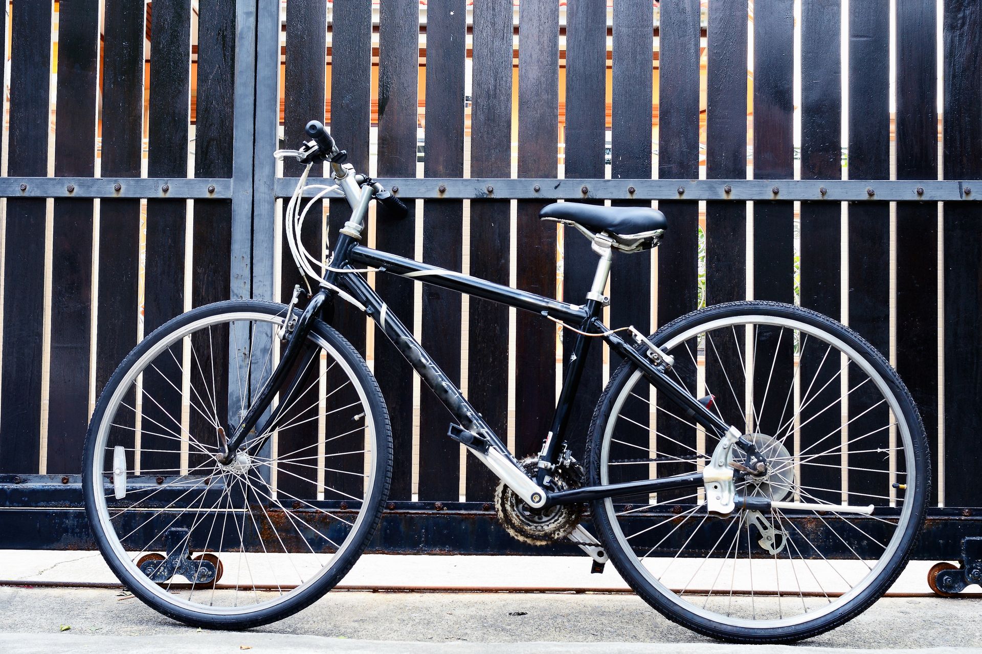 Black bicycle parked in front of a dark wooden gate.