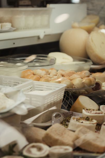Formaggi assortiti e cracker esposti su un banco di mercato o di gastronomia con cestini e vassoi.