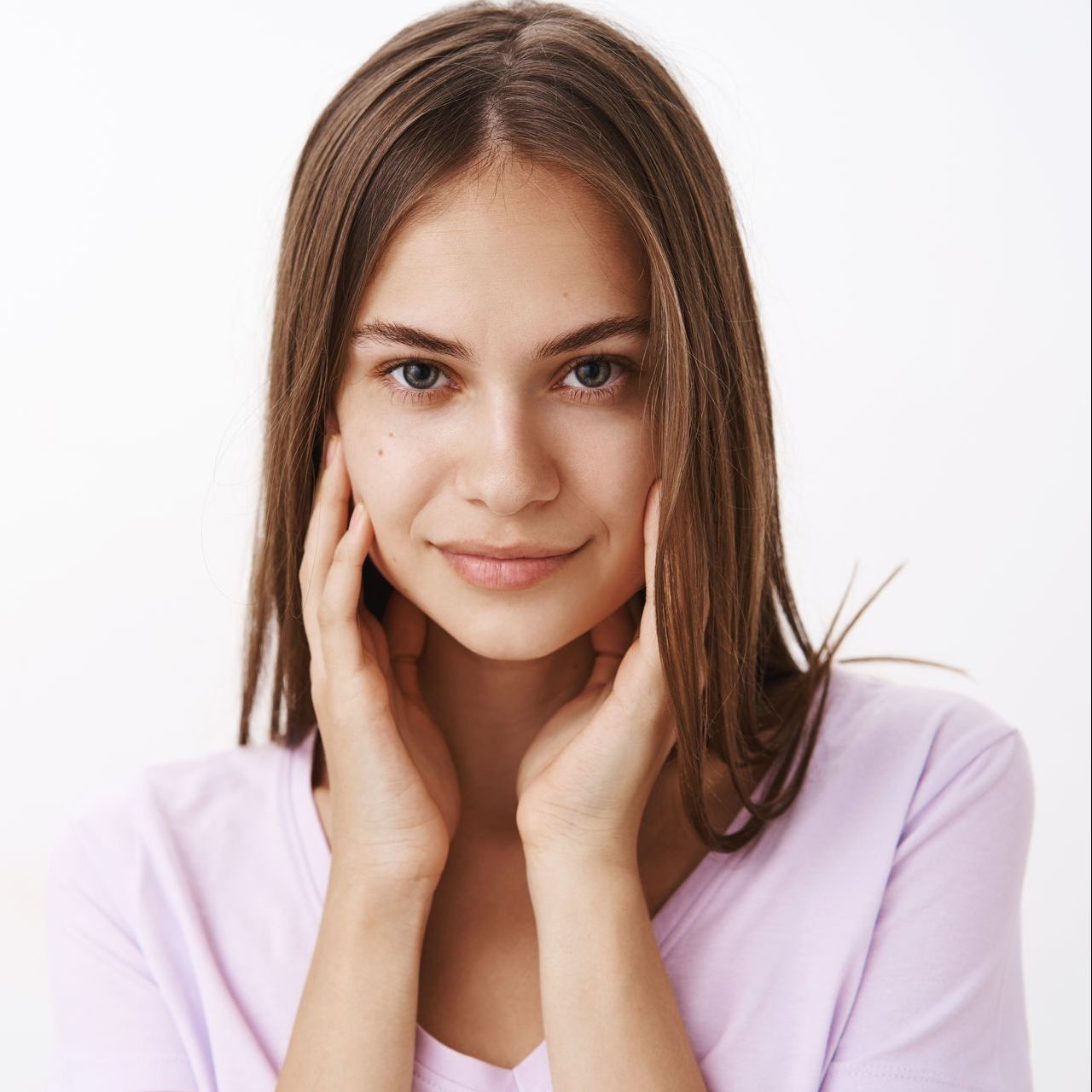 A woman is touching her face with her hands and smiling.
