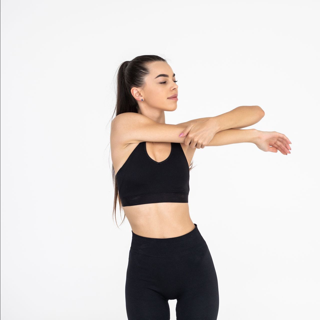 A woman in a black crop top and black leggings is stretching her arms.