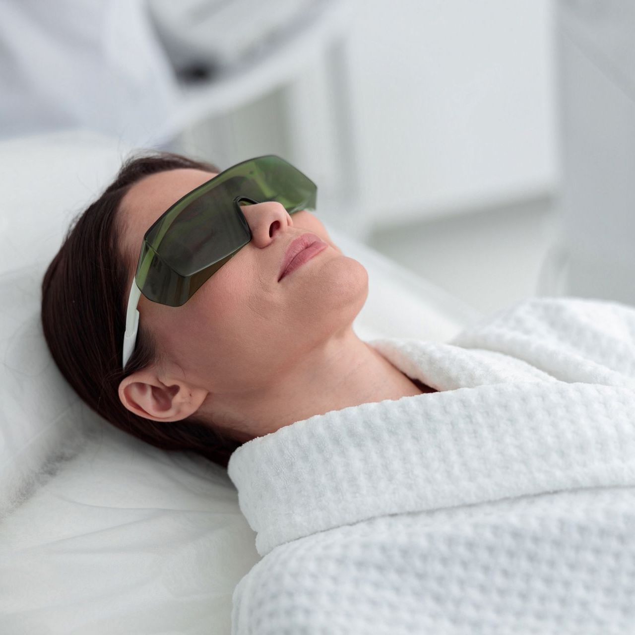 A woman wearing sunglasses is laying on a bed.