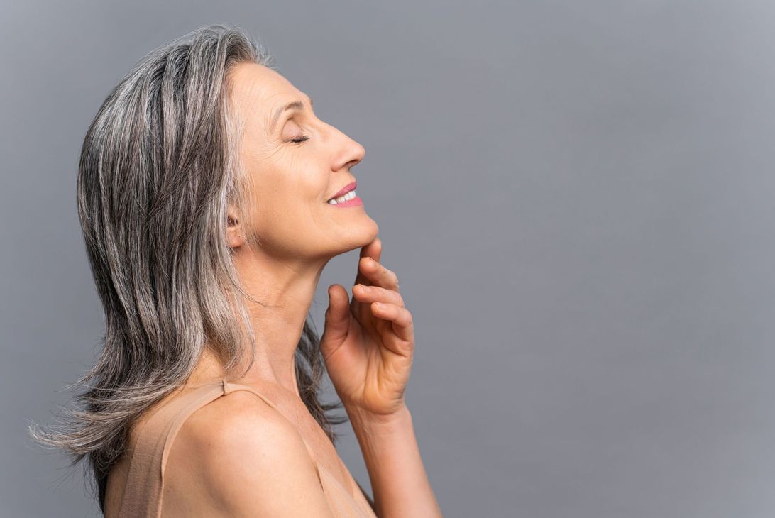 A woman performs a cosmetic procedure on a client lying down. The setting is a beauty clinic with specialized equipment.