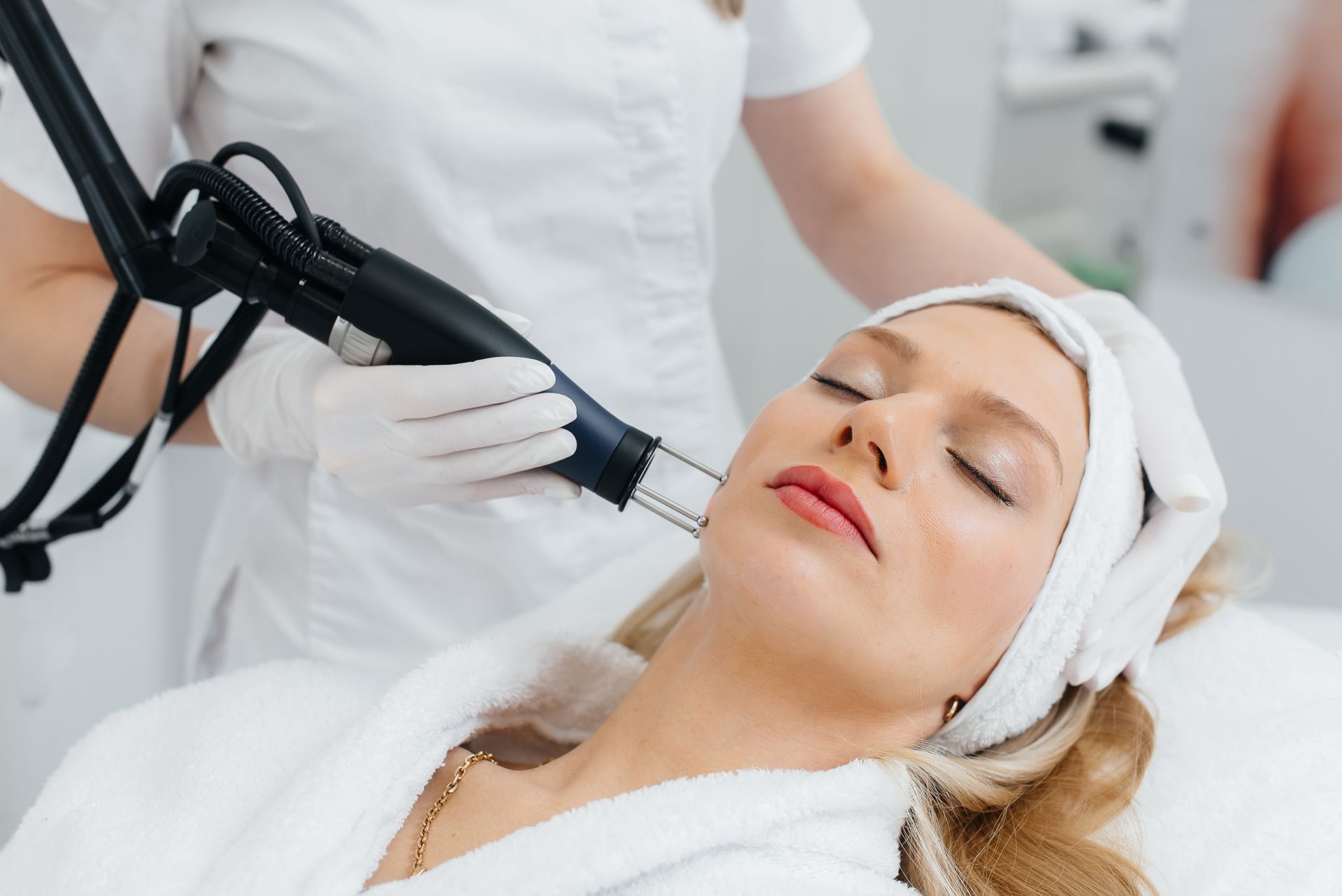 Woman receiving laser treatment on her face at a spa; technician holding the device.