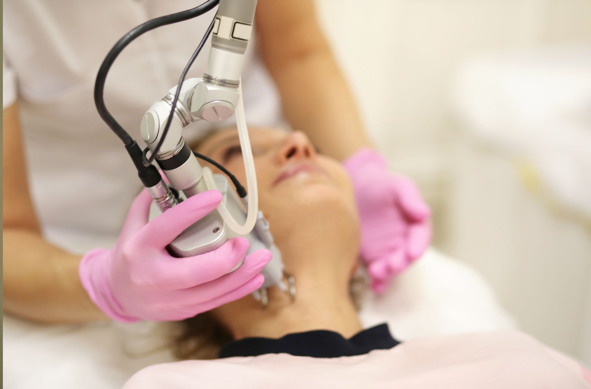 Woman receiving laser skin treatment from a gloved professional, in a medical setting.