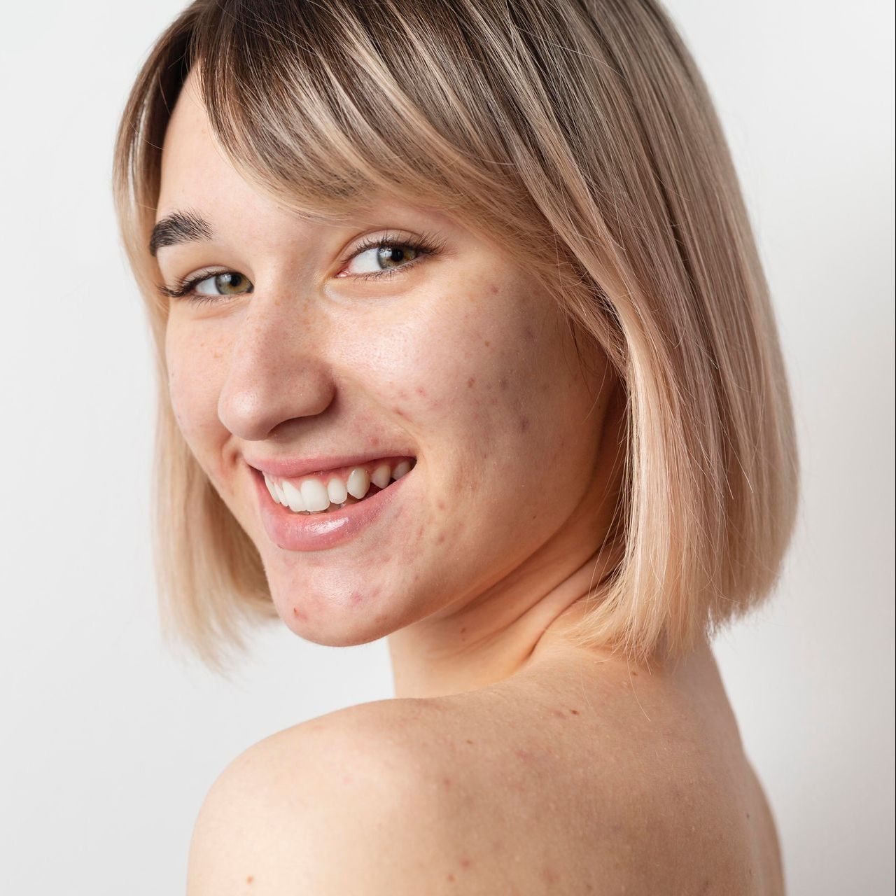 A woman with blonde hair is smiling and looking over her shoulder