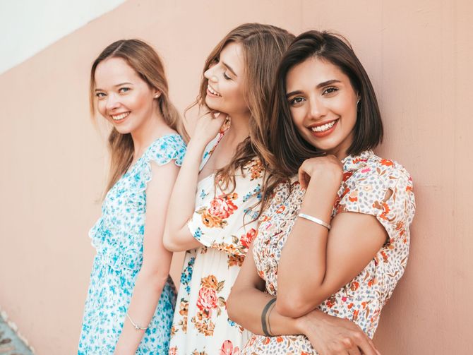 Three women in dresses are standing next to each other and smiling.