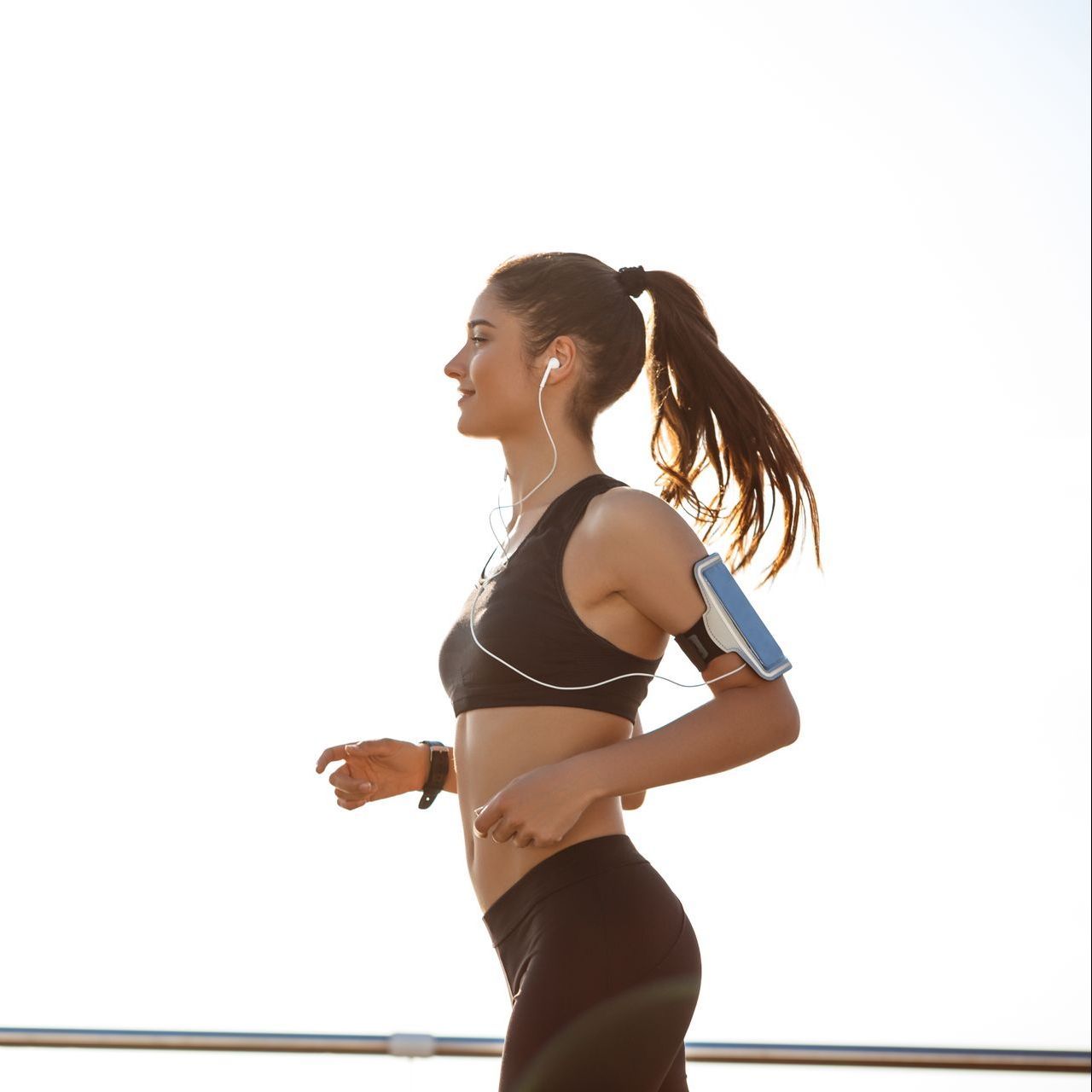 A woman is running on the beach with a cell phone in her pocket.