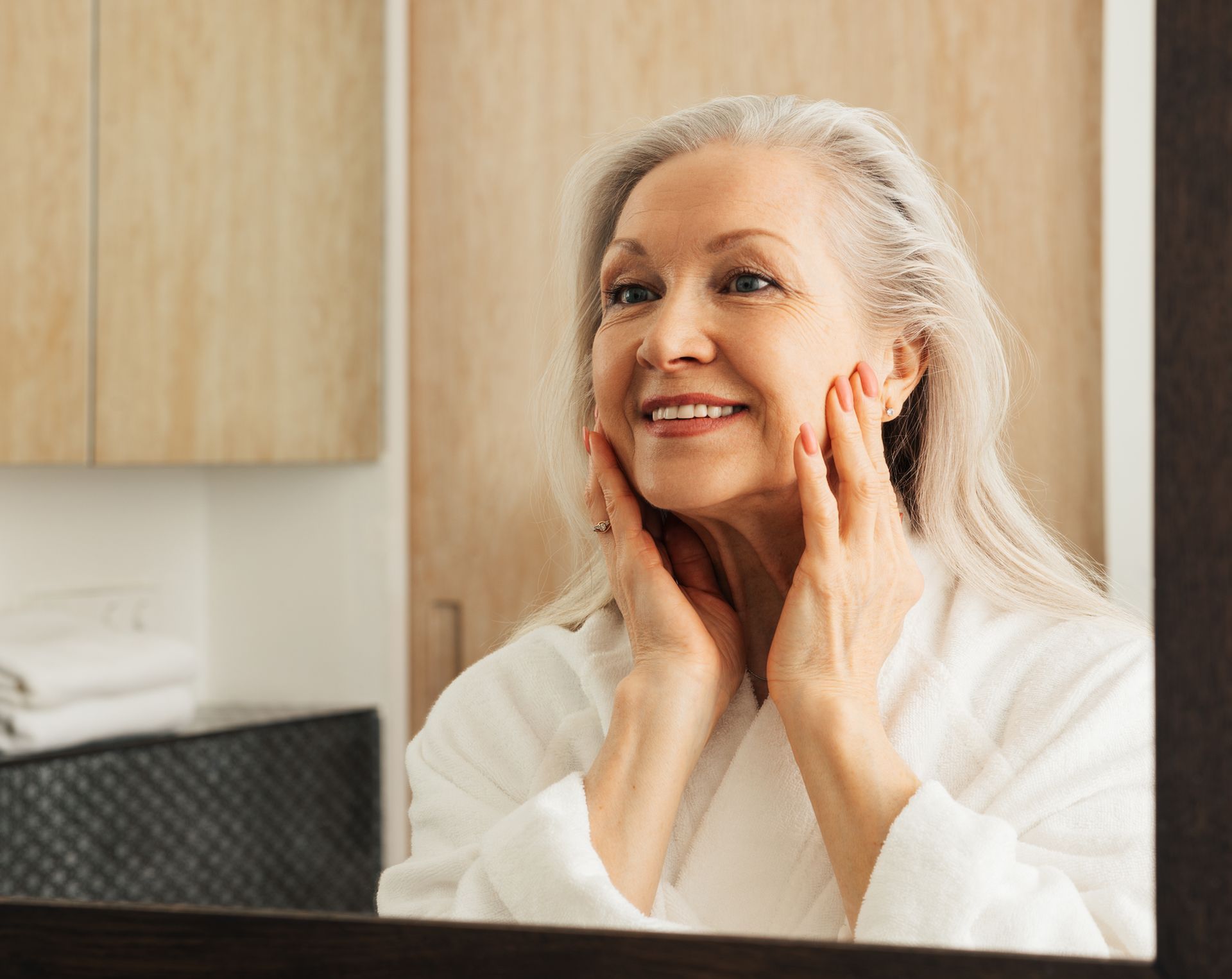 An older woman is looking at her face in a bathroom mirror.