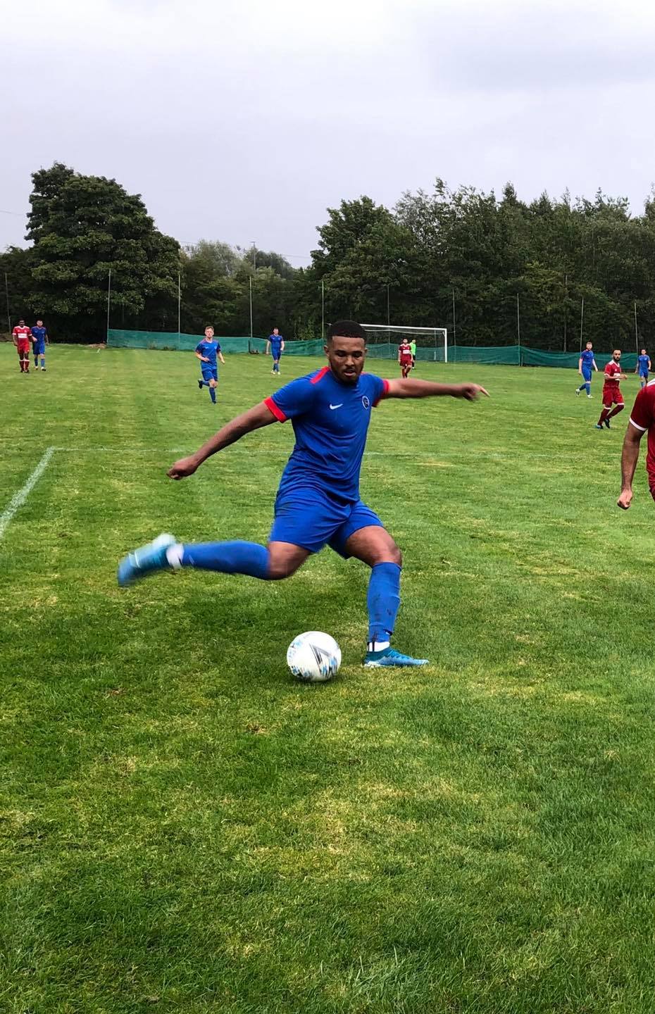 A man in a blue shirt is kicking a soccer ball on a field.