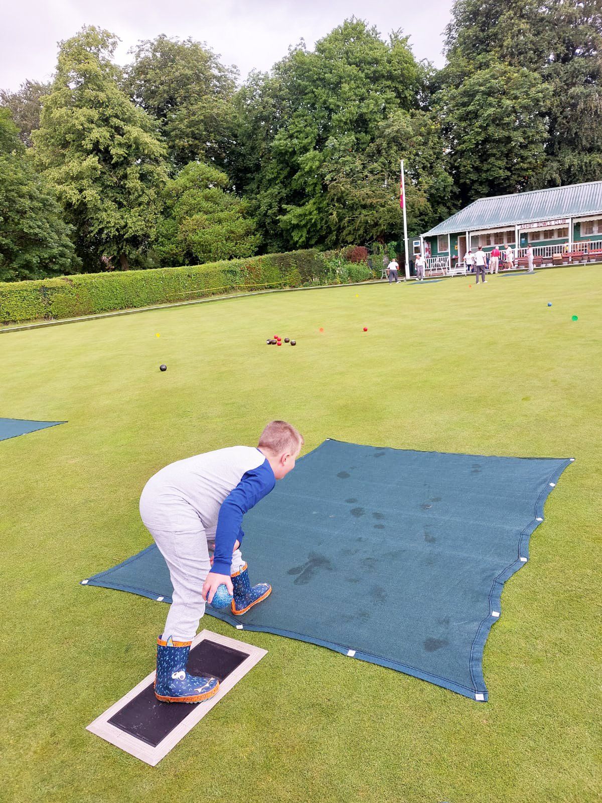 A young boy is standing on a green mat on a lush green field.