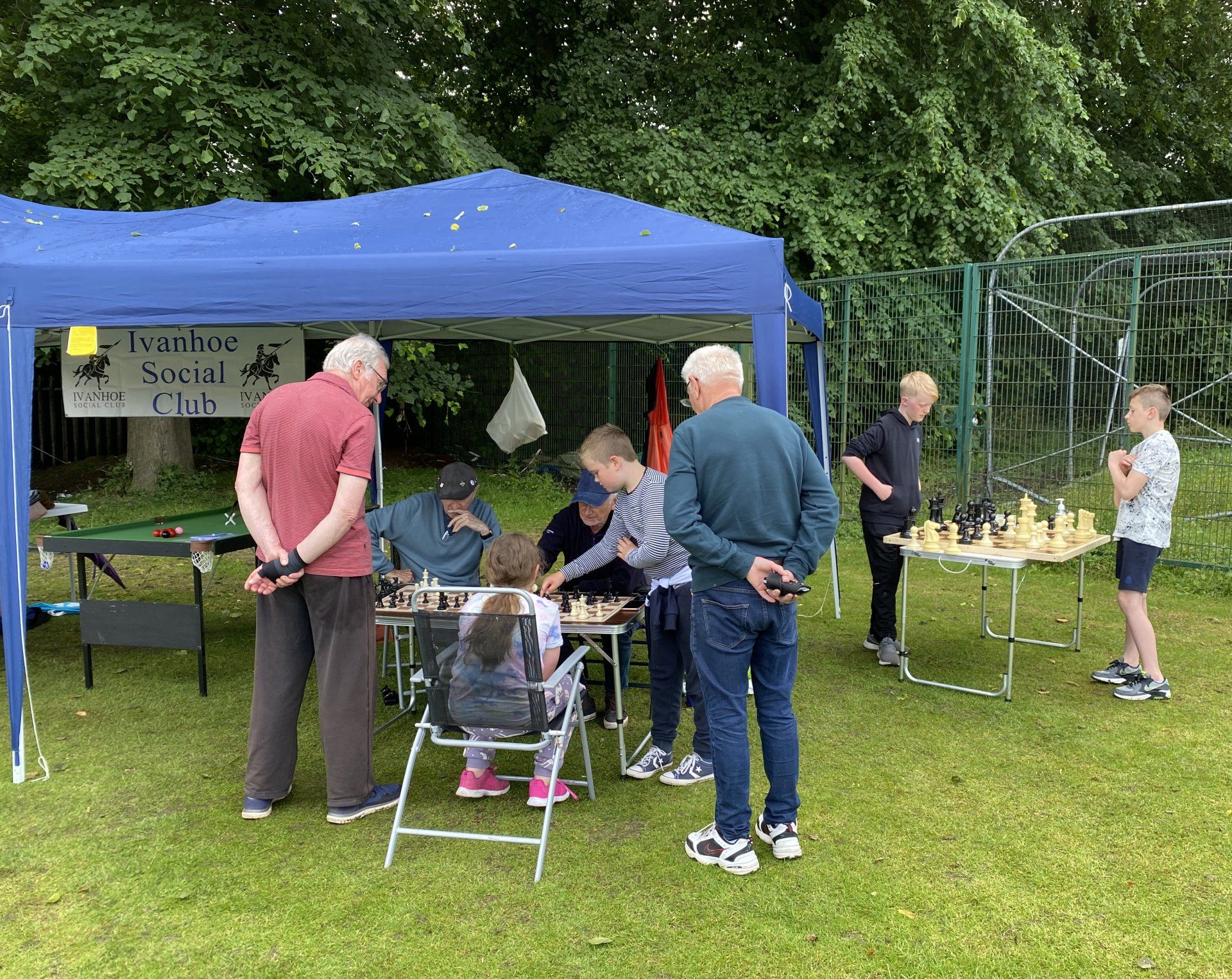 A group of people are playing chess under a blue tent.