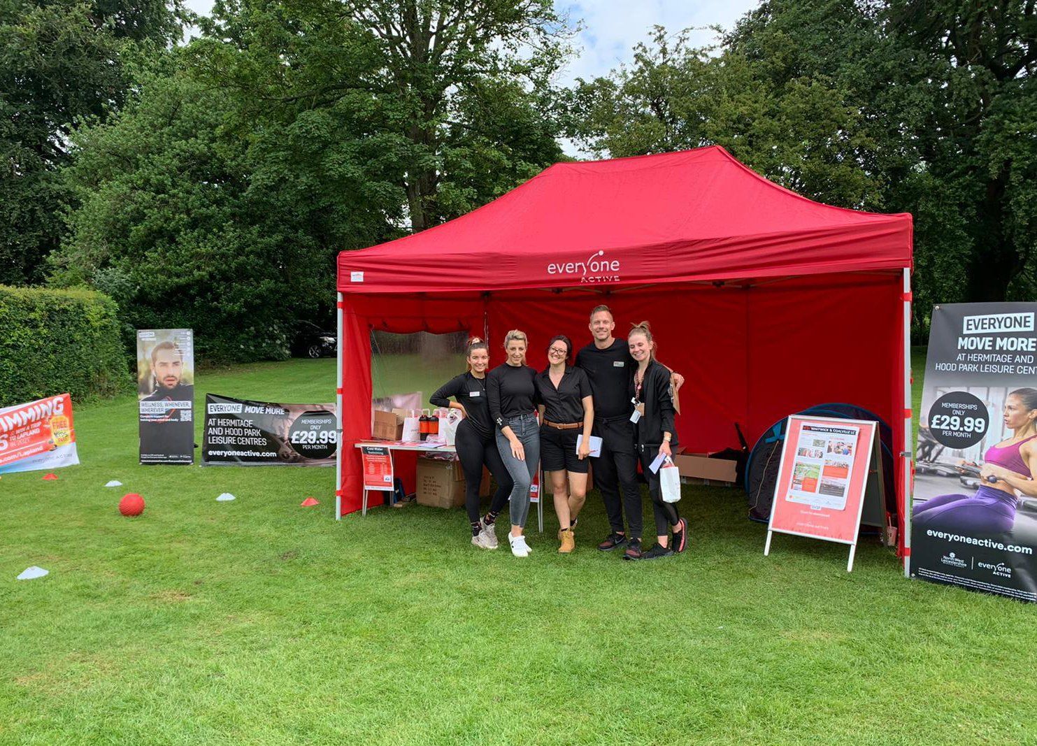 A group of people standing in front of a red tent in a park.