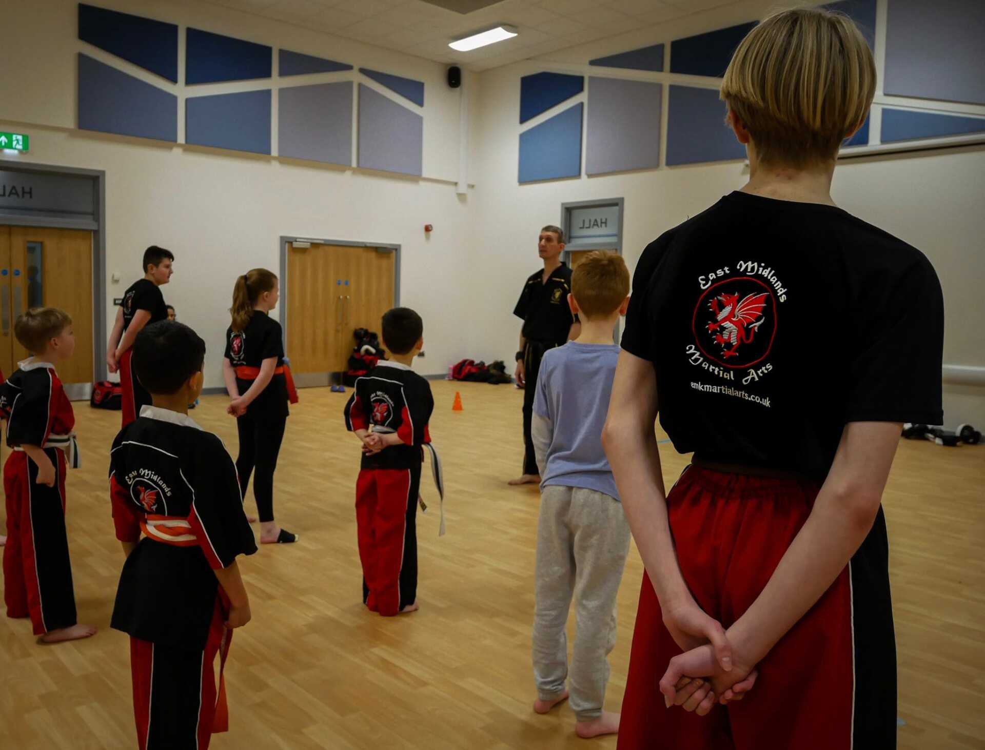 A group of kids are standing in a room and one of them is wearing a black shirt with a dragon on the back