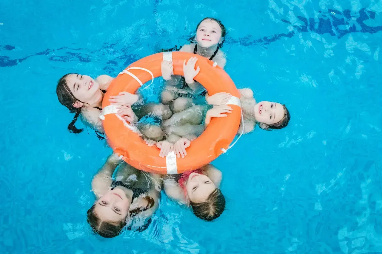 A group of children are swimming in a pool holding a life preserver.