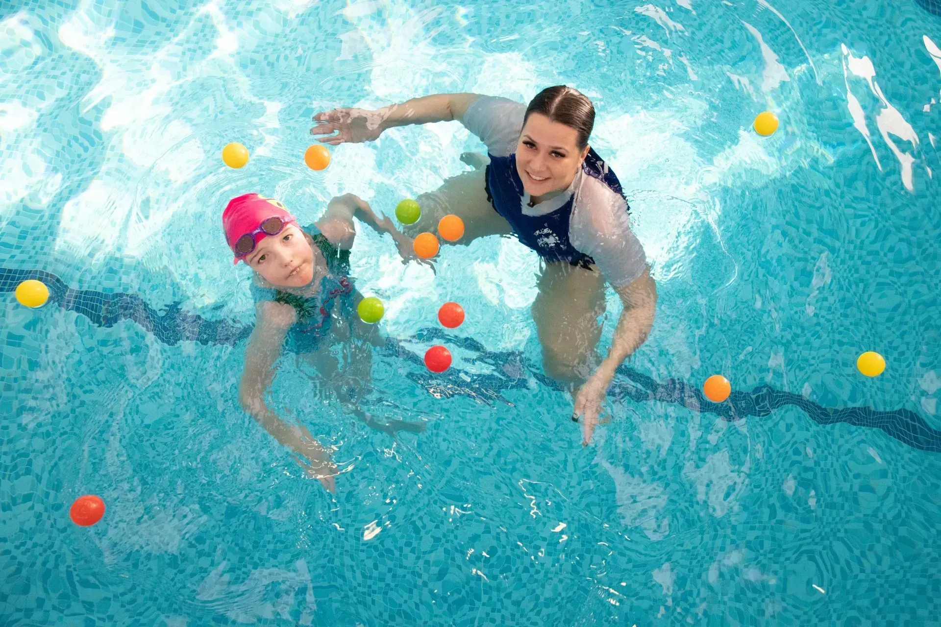 A woman and a child are playing with balls in a swimming pool.
