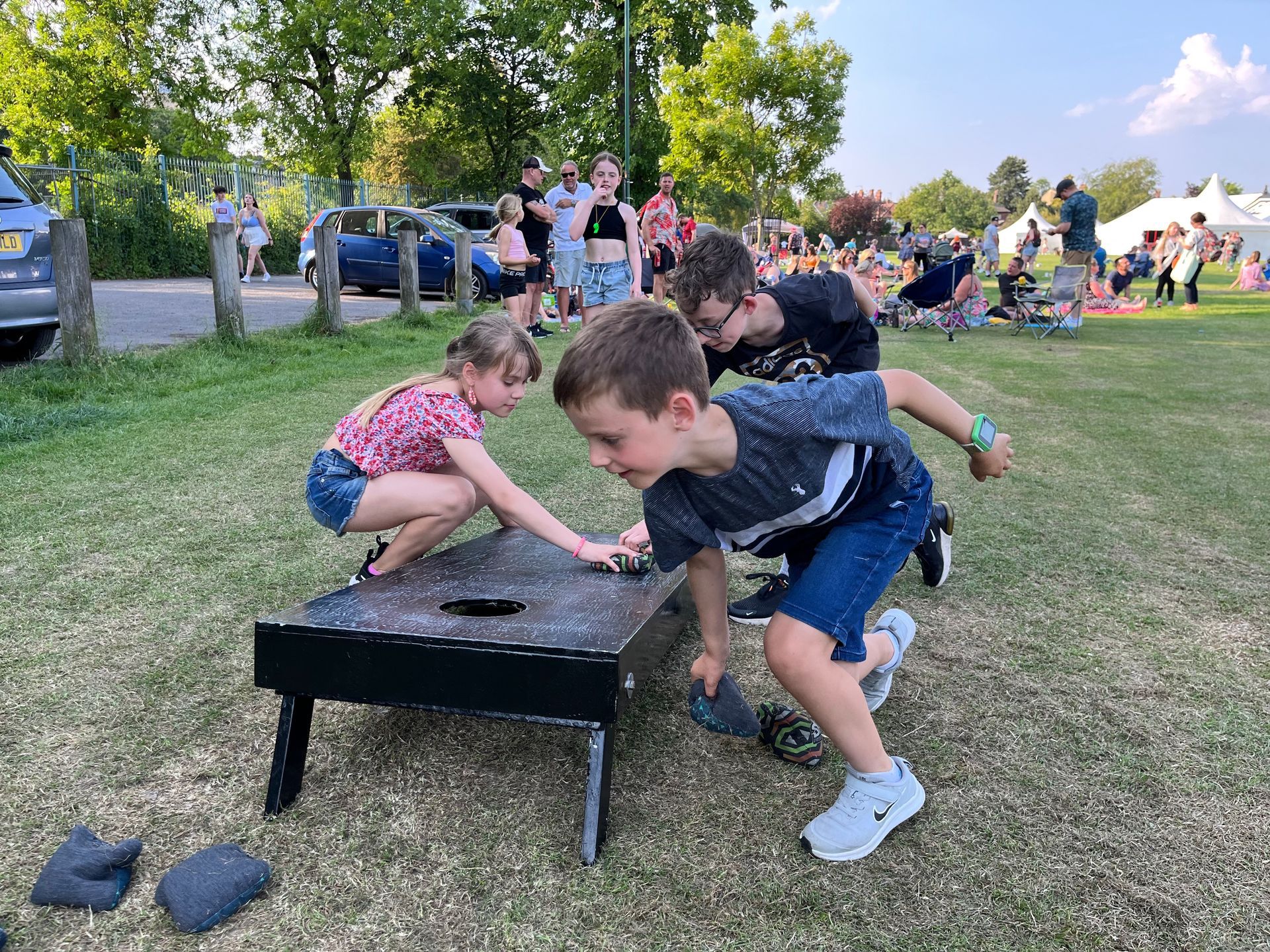 A group of children are playing a game of cornhole in a park.