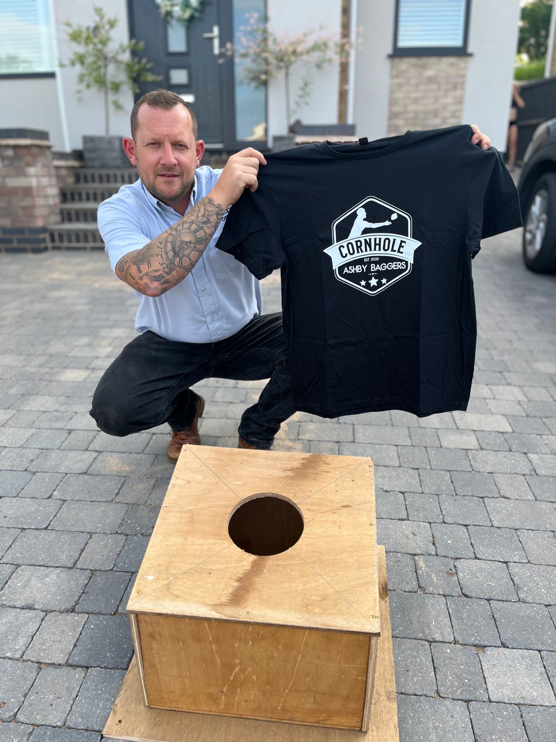 A man is kneeling down holding a black shirt over a wooden box.