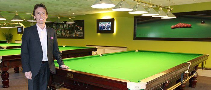 A man in a suit is standing in front of a pool table.