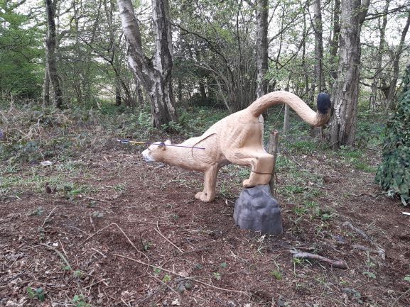 A statue of a lion is standing on a rock in the woods.