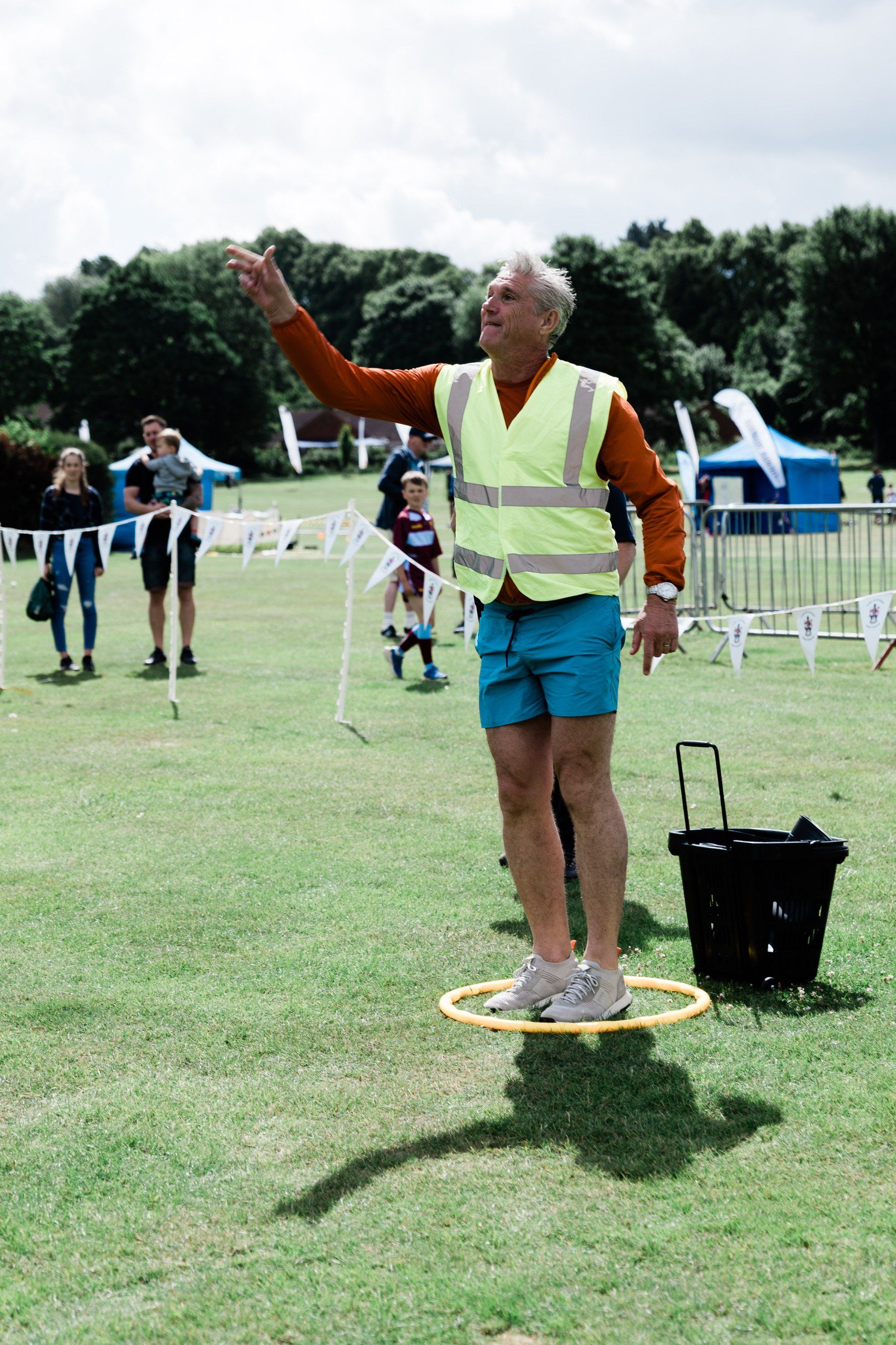 A man in a yellow vest is standing on a hula hoop in a field.