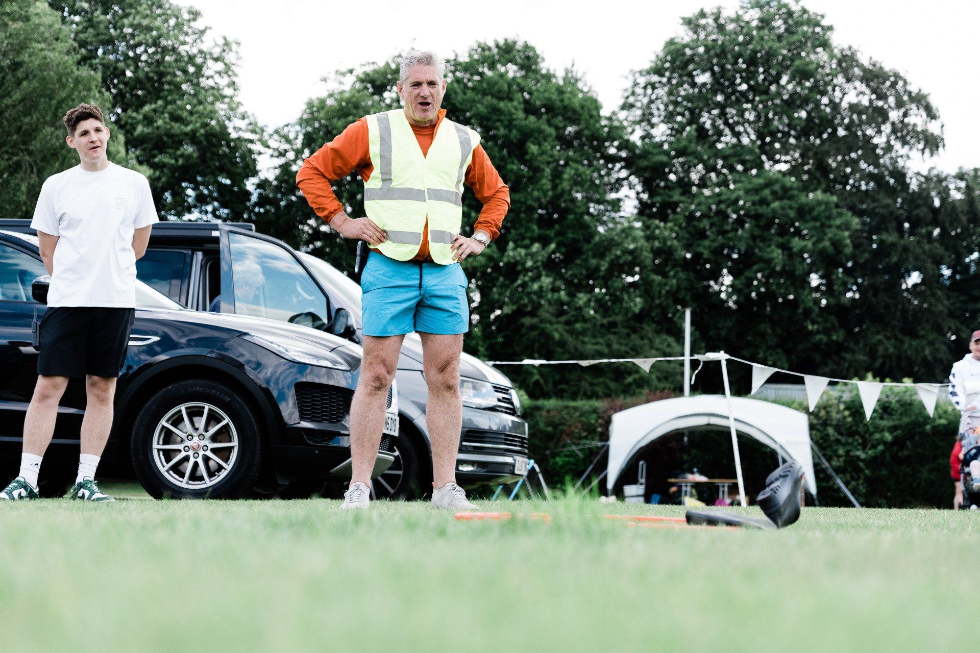A man in a yellow vest is standing in a field next to a car.