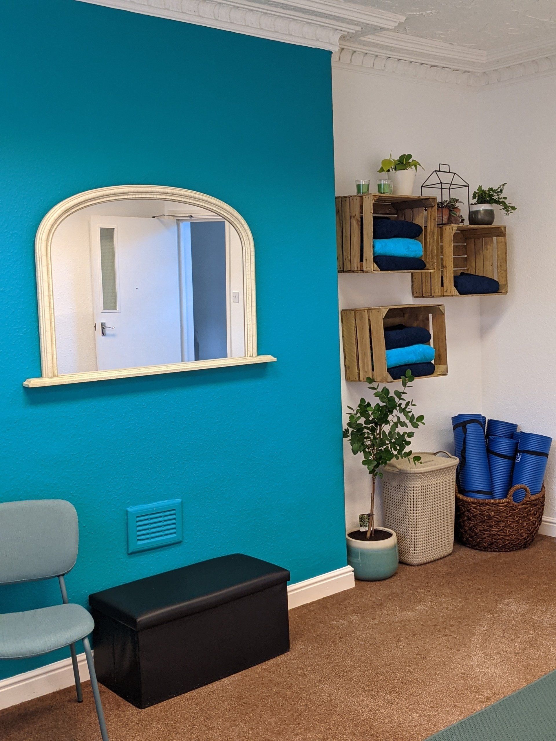 A room with a blue wall , a chair , a bench and a mirror.