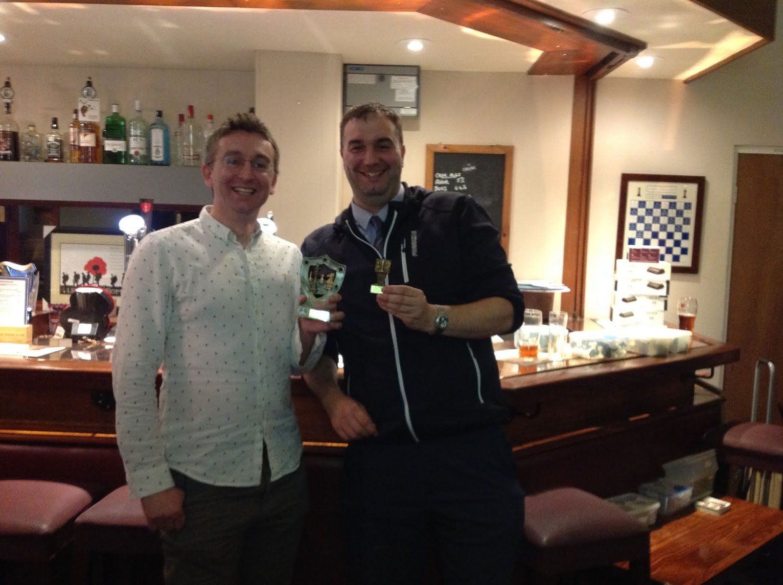 Two men standing next to each other in a bar holding medals