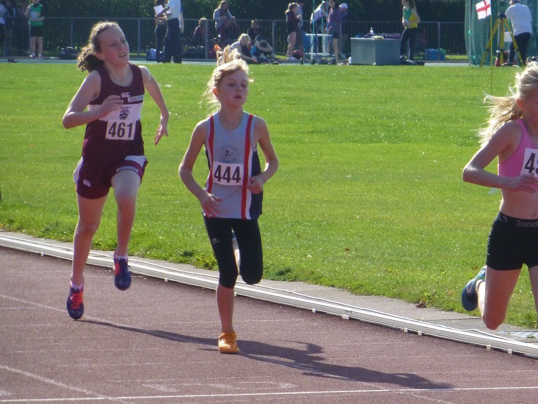 Three girls are running on a track and one has the number 444 on her shirt