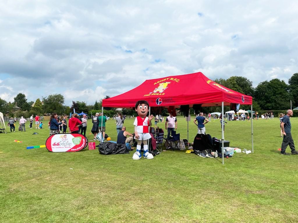 A mascot is standing under a red tent in a field.