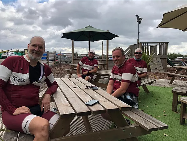 A group of men are sitting at a picnic table under an umbrella.