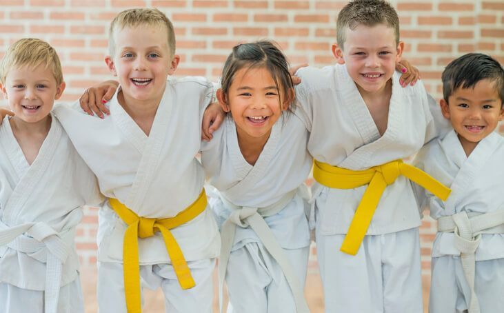 A group of children wearing karate uniforms and yellow belts are posing for a picture.