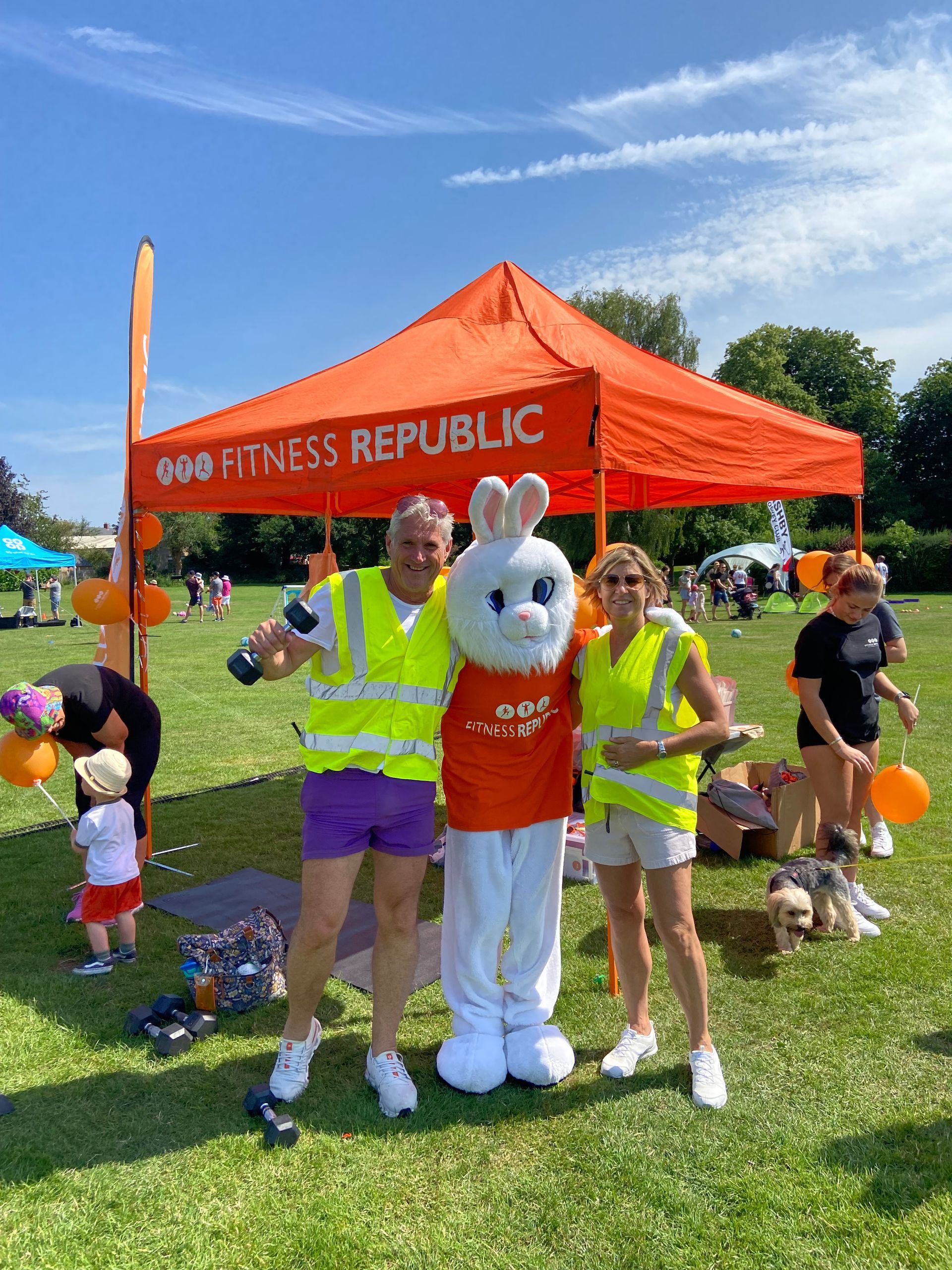 A group of people standing next to a mascot under an orange tent.