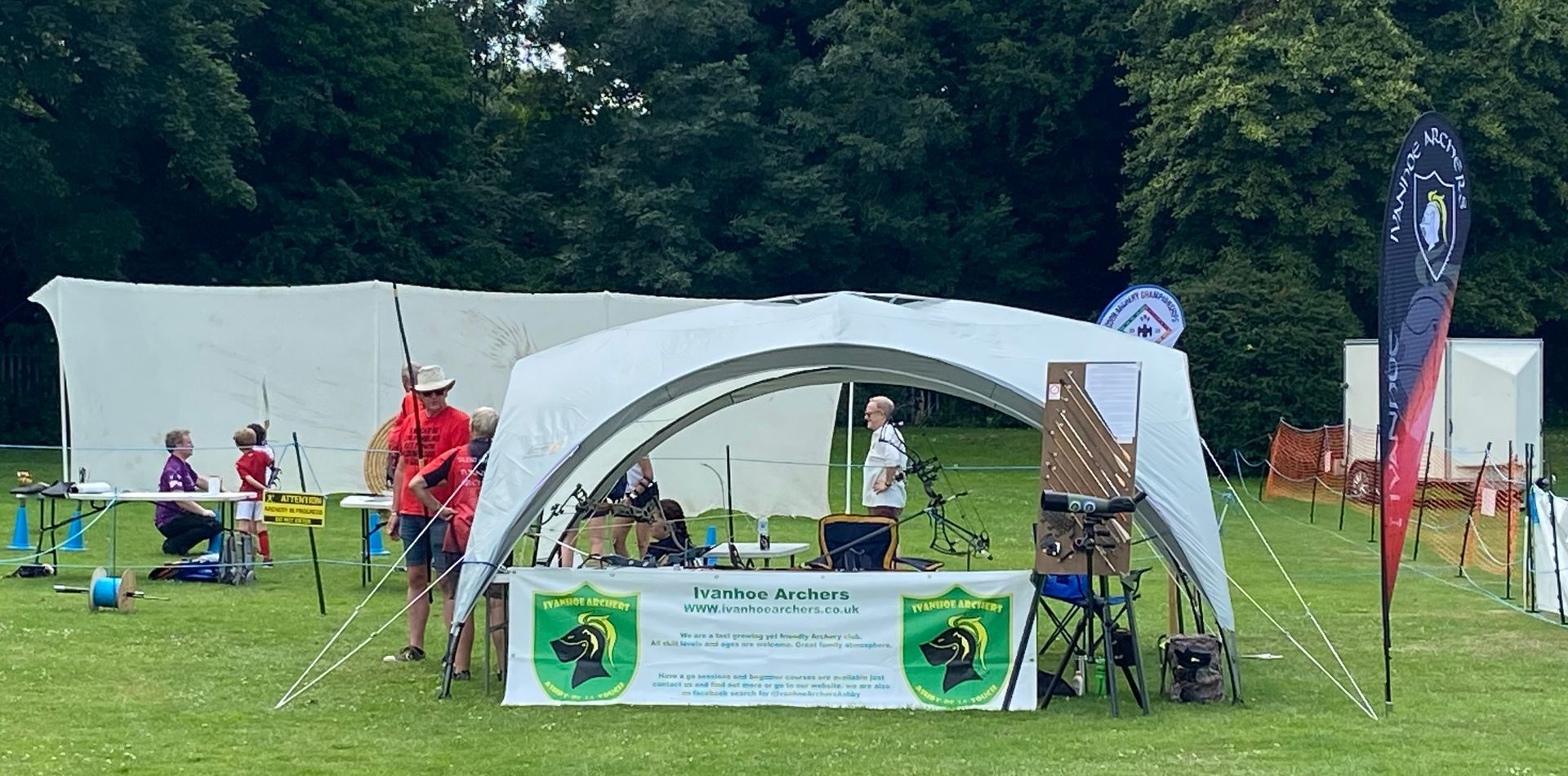 A group of people are standing under a tent in a field.