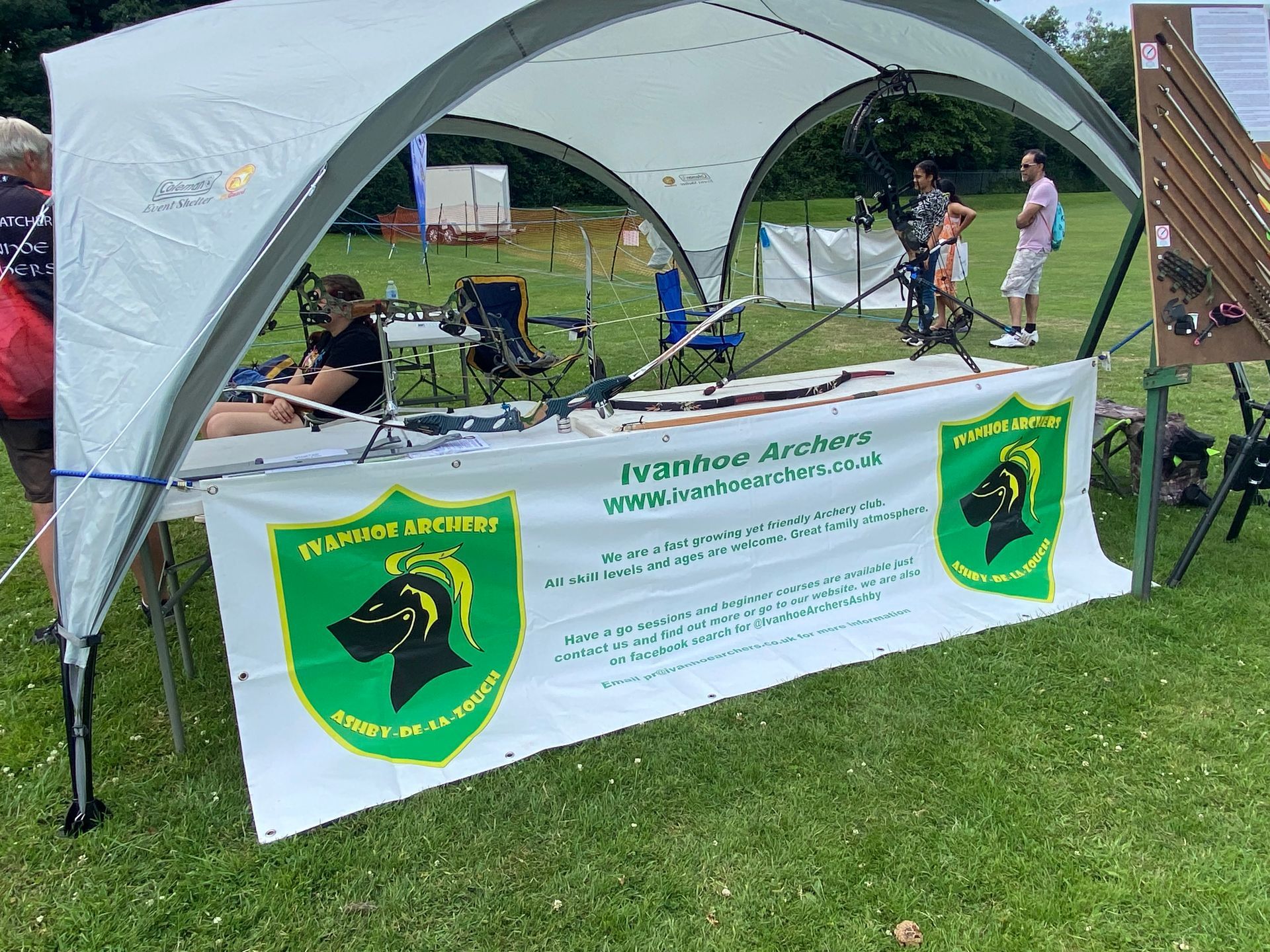A man is sitting at a table under a tent in a field.