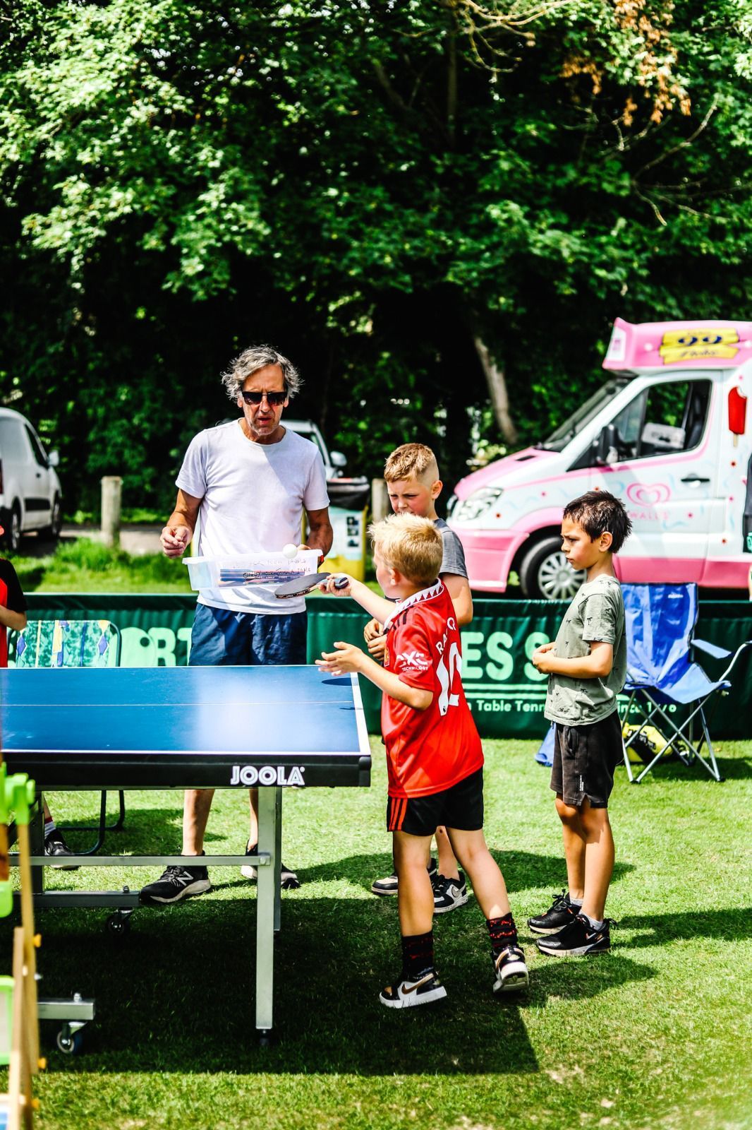 A group of young boys are playing ping pong in front of an ice cream truck.