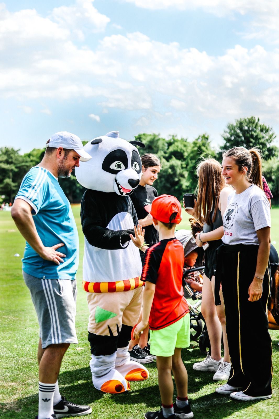 A group of people are standing in a field with a panda mascot.