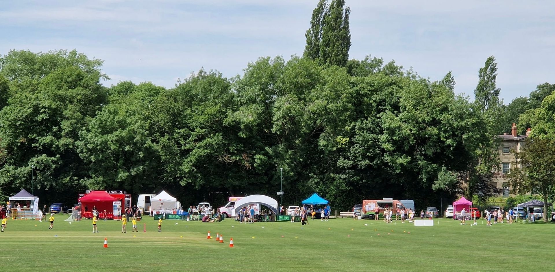 A row of tents in a grassy field with trees in the background