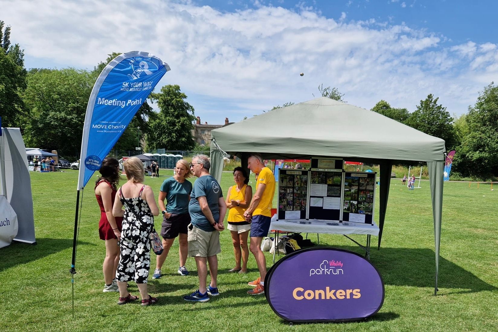 A group of people are standing around a tent in a park.