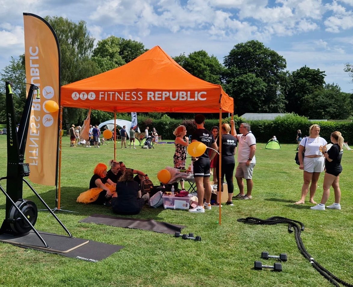 A group of people are standing under an orange tent that says fitness republic.