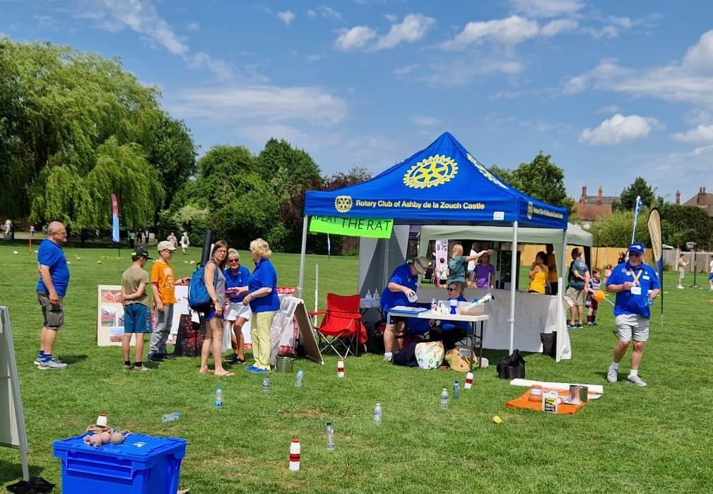 A group of people are standing around a blue tent in a park.