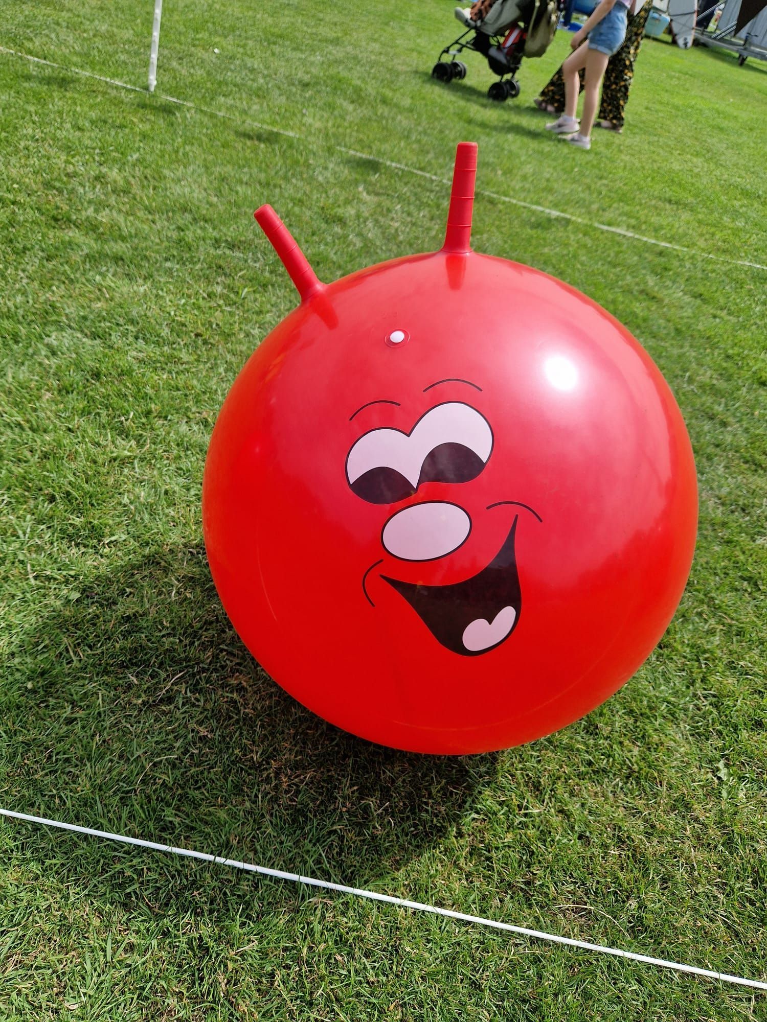 A red jumping ball with a face on it is sitting on the grass.
