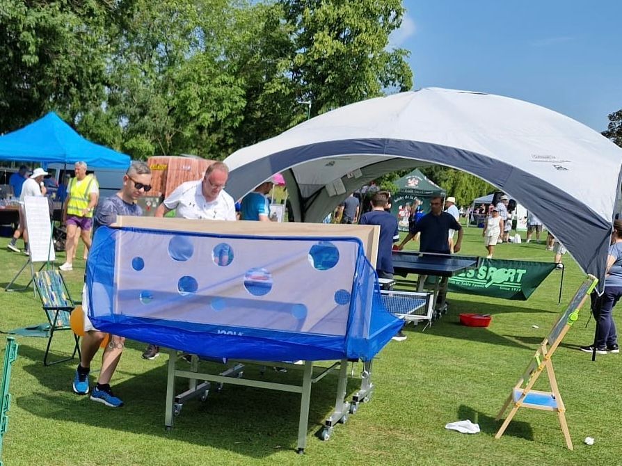 A group of people are playing ping pong in a park under a tent.