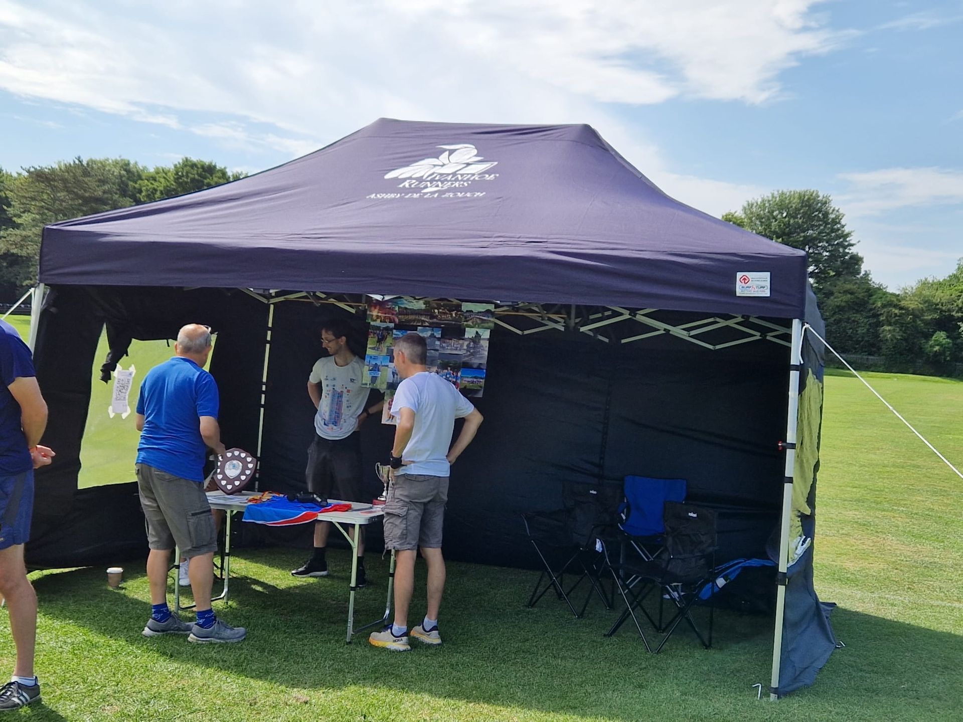 A group of people are standing under a tent in a field.