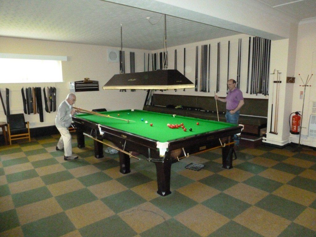 Two men are playing pool in a room with a checkered floor