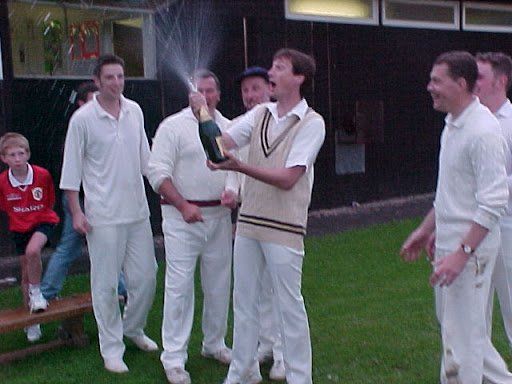 A man holding a bottle of champagne is surrounded by other men