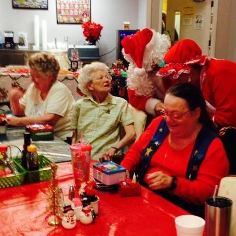 A group of people are sitting at a table and one of them is dressed as santa claus