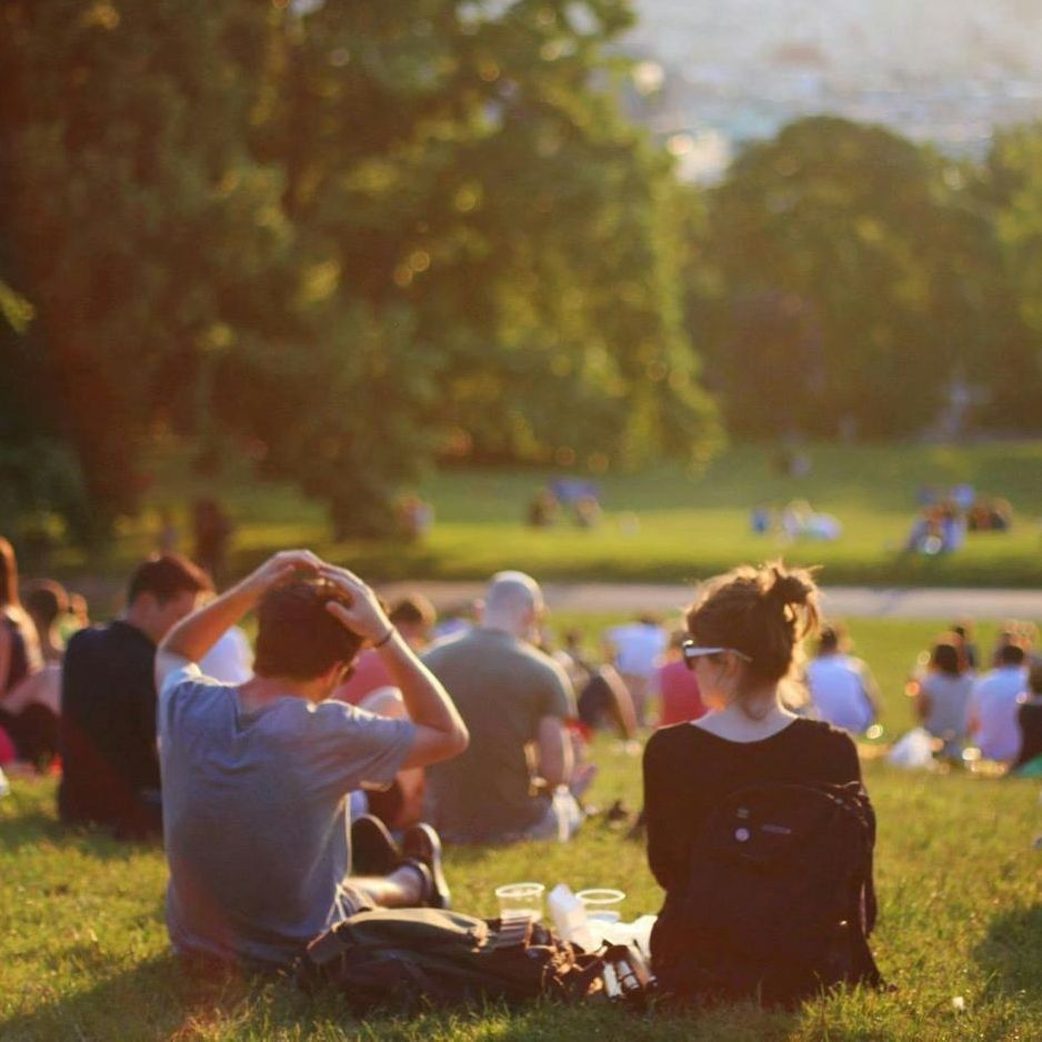 A group of people are sitting in the grass in a park.