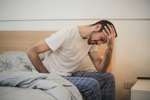 A man is sitting on a bed with his hand on his head.